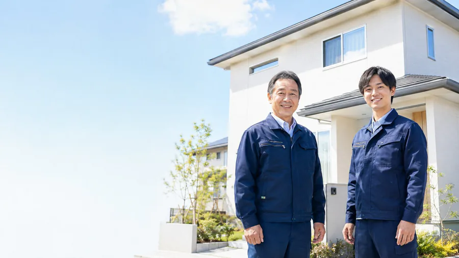 住宅の前に立つ作業服のスタッフ2人（イメージ）